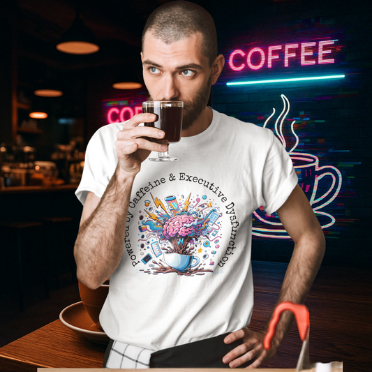 Man drinking coffee at a trendy café while wearing a “Powered by Caffeine & Executive Dysfunction” t-shirt by Mentally Glitched.